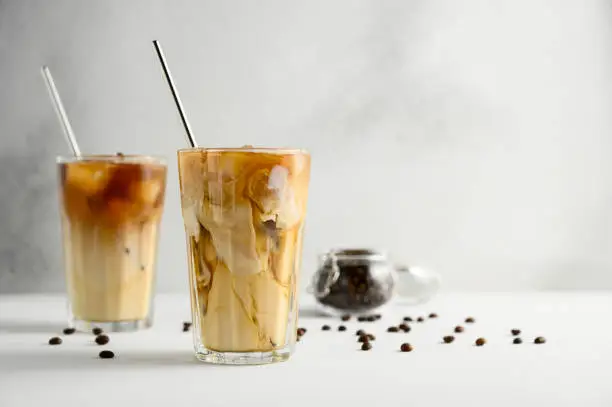 Photo of Two glasses of iced coffee on a light concrete table.