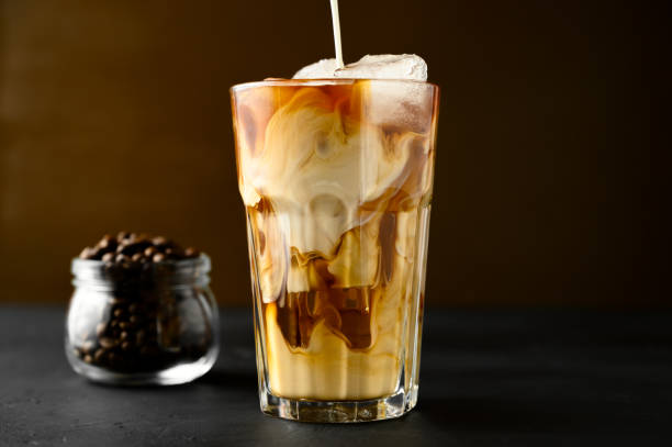 istock Milk is poured into a transparent glass with iced coffee on a black table. 1218361899