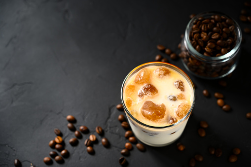 Iced coffee in a glass cup on a black concrete table. Top view, copy space.