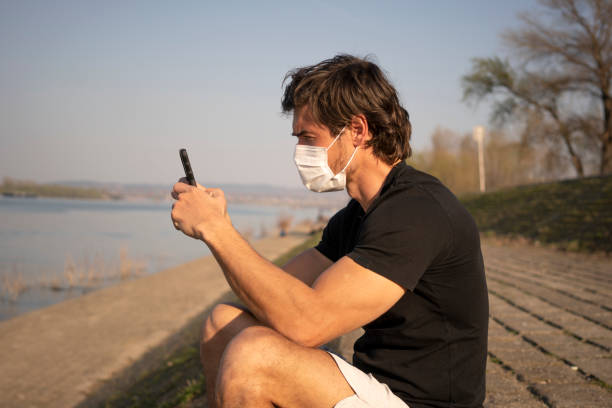 El hombre usa máscara para prevenir virus y para la protección mientras usa el teléfono móvil - foto de stock