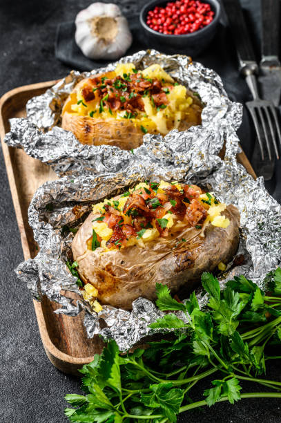 istock Two baked potatoes with bacon, green onion and cheese. Black background. Top view 1218364907