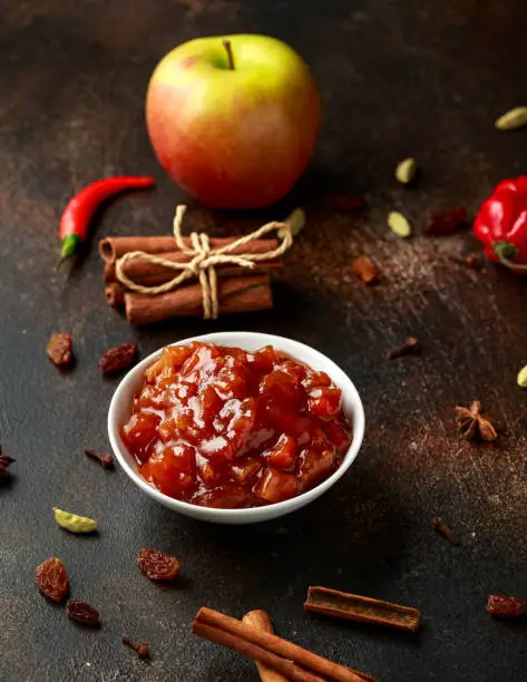 Homemade apple and chilli chutney with spices on dark background.