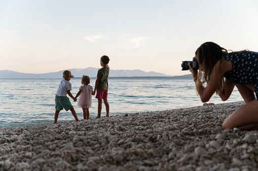 Capturing Rovinj's beauty,A female tourist focused behind her SLR camera,photographing against the clear blue sky and the old town by the sea in Rovinj,Croatia. A blend of technology and artistry in a picturesque coastal setting