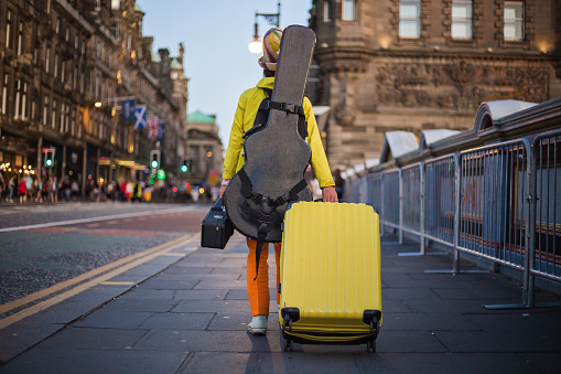 Traveling musician carrying a yellow suitcase and a guitar case while traveling.