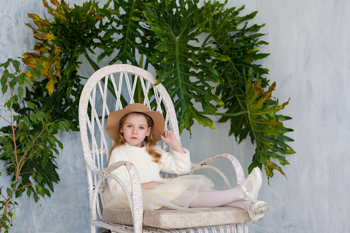 Little girl in a hat sits in a white chair
