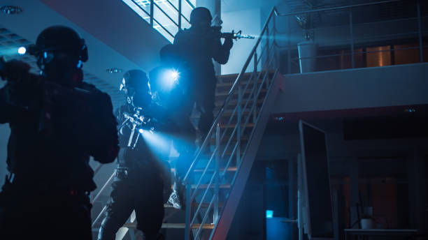 escuadrón enmascarado de oficiales de policía swat armados corren por las escaleras desde un segundo piso en un edificio de la oficina oscura. los soldados con rifles y linternas avanzan y cubren los alrededores. - black ops fotografías e imágenes de stock