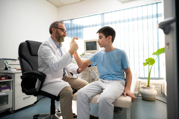 ragazzo muove il braccio con l'assistenza di un medico - doctor patient doctors office teenager foto e immagini stock