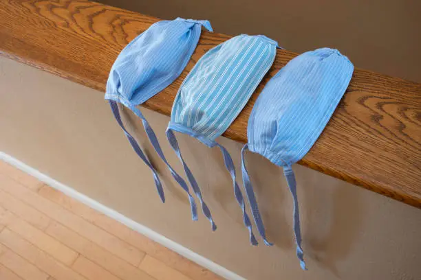 A close-up of three, hand-sewn face masks that were made from blue striped cotton cloth, without elastic-bands, to help prevent the spread of the COVID-19 virus that has plagued the world.