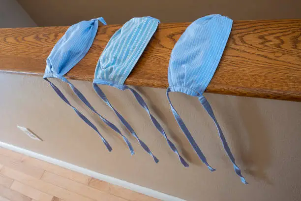 A close-up of three, hand-sewn face masks that were made from blue striped cotton cloth, without elastic-bands, to help prevent the spread of the COVID-19 virus that has plagued the world.