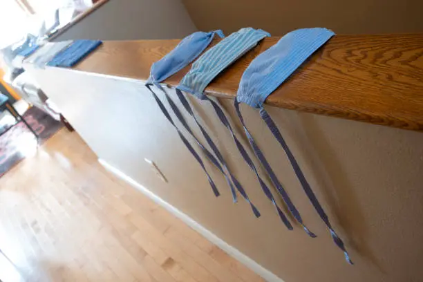 A close-up of three, hand-sewn face masks that were made from blue striped cotton cloth, without elastic-bands, to help prevent the spread of the COVID-19 virus that has plagued the world.