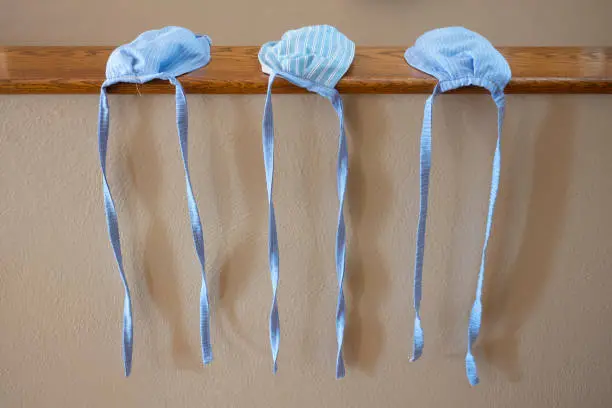 A close-up of three, hand-sewn face masks that were made from blue striped cotton cloth, without elastic-bands, to help prevent the spread of the COVID-19 virus that has plagued the world.