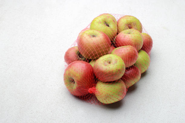 istock Small apples in a plastic mesh sack on a white background 1218384873