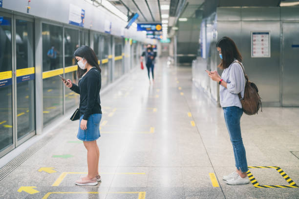 Two young asian woman wearing protective face mask stand in line with social distancing during waiting train in subway due to Coronavirus or COVID-19 outbreak situation in all of landmass in the world Two young asian woman wearing protective face mask stand in line with social distancing during waiting train in subway due to Coronavirus or COVID-19 outbreak situation in all of landmass in the world landmass stock pictures, royalty-free photos & images