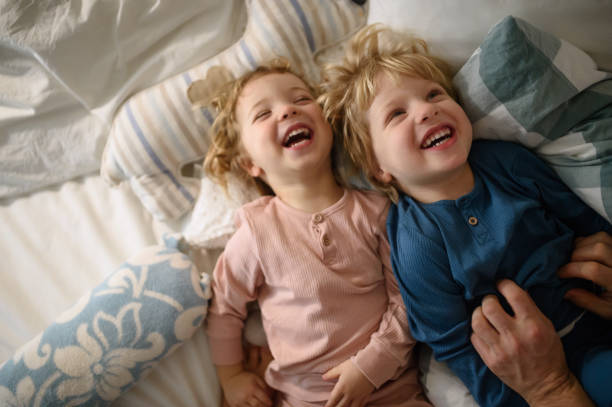 duas crianças rindo com o pai irreconhecível em casa, se divertindo. - offspring child lying on back parent - fotografias e filmes do acervo