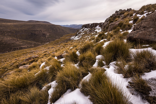 A tranquil snow-covered mountain landscape with snow and grass in the foreground, taken in Lesotho South Africa, on a stormy, cloudy afternoon.