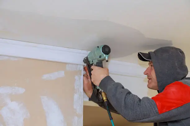 Carpenter using air nail gun to crown moldings trim for ceiling