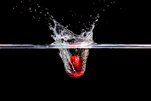 A studio shot of a strawberry splashing into water.