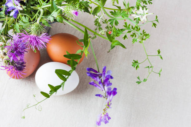 Tre multi-colored chicken eggs on a linen tablecloth with a bouquet of spring wildflowers. Ester concept. Easter greeting card.