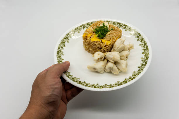 istock Hand serving Fried rice with egg along with premium lump crab meat and topped with chopped spring onion. Favorite Thai seafood dish isolated on white background. 1218404757