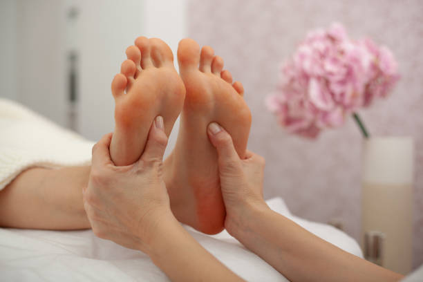 vista ritagliata del massaggiatore che fa massaggio ai piedi alla donna adulta nel salone di bellezza - foot massage foto e immagini stock