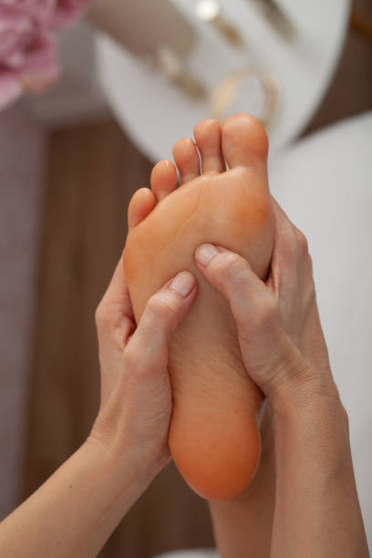 vue cultivée du masseur faisant le massage de pied à la femme adulte dans le salon de beauté - reflexology pedicure massaging human foot photos et images de collection