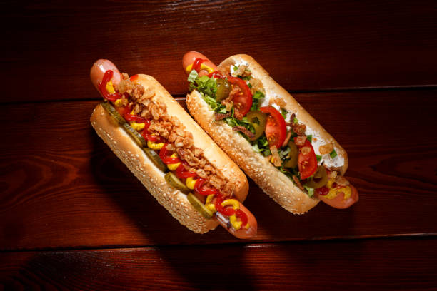 Danish hot dog with pickled cucumbers, fried onions and a hot dog with soft cheese, tomatoes and jalapenos on a wooden table. View from above. stock photo