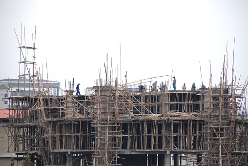 Addis Abeba, Ethiopia, 06/30/2007. Close-up of the highest floors with scaffolding made with tree trunks in a plant building and concrete columns under construction. Ethiopian workers on the top floor construction site. Office and business building.