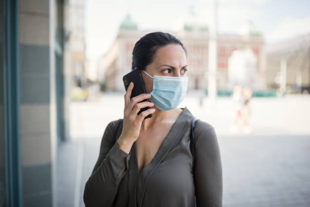 istock Woman wearing protective mask, using mobile phone 1218419433