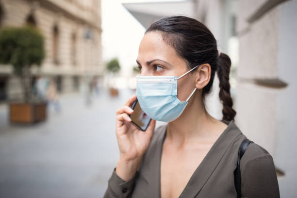 istock Woman wearing protective mask, using mobile phone 1218419641