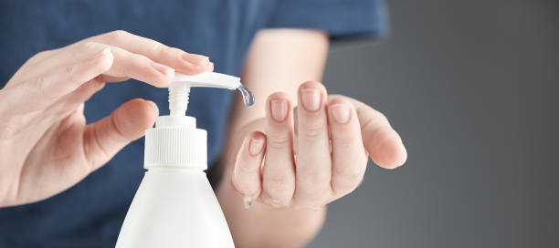 istock Female hands using hand sanitizer gel pump dispenser on a gray background. 1218425062