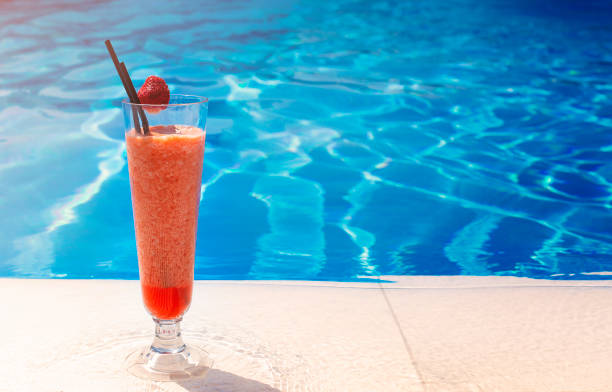 vidro com um coquetel vermelho brilhante na mesa à beira da piscina com espaço de cópia - strawberry mocktail smoothie cocktail - fotografias e filmes do acervo
