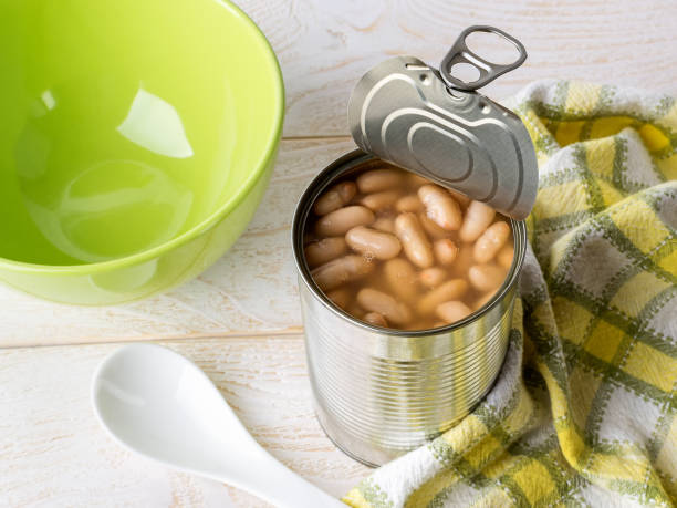 istock Canned backed beans in an open tin can with pull tab near ceramic bowl and spoon on a wood table. Bean is source of vegetable protein and ingredient for vegetarian food. 1218430350