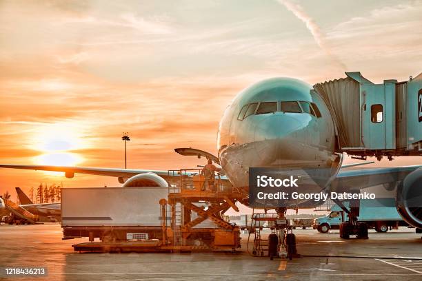 Modern Passenger Airplane Parked To Terminal Building Gate At Airside Apron Of Airport With Close Up Airplane Parts Jet Engine Wing Windows Gear Tow Tractor Noon Sun View Stock Photo - Download Image Now