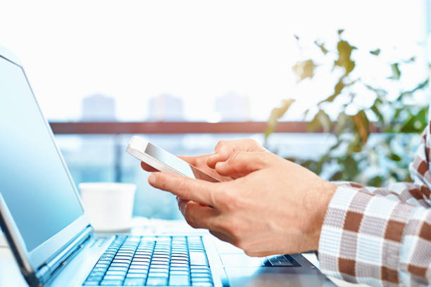 istock Close-up shot of an unrecognizable man holding his smart phone while using a laptop 1218436309