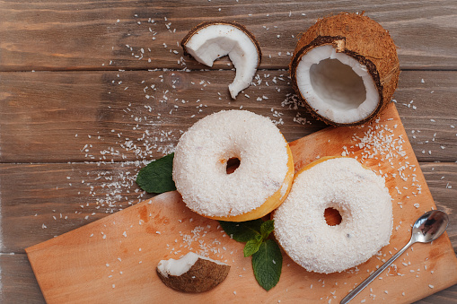 two large coconut donuts on a cutting board with mint leaves and coconut pieces laid out nearby