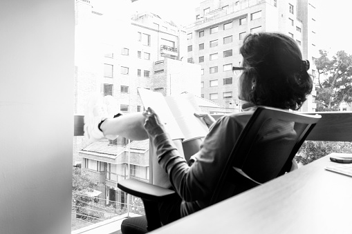 Girl reading under the light that enters through a panoramic window, where you can see the street, the buildings around and part of the room
Series of images about an activity carried out during social isolation
Black and White image