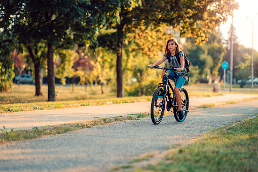 Girl wearing stripe shirt and backpack riding a bike on a sunny day