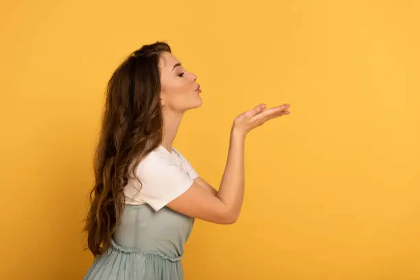 Photo of beautiful elegant spring girl blowing air kiss on yellow