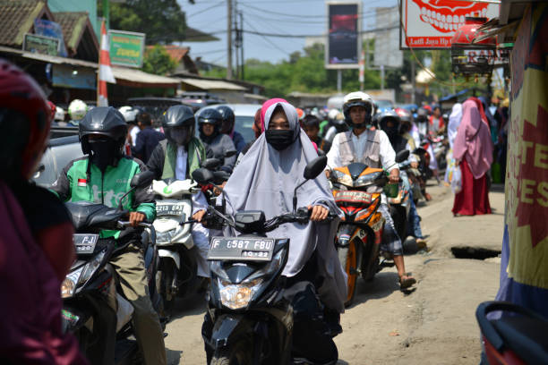 Locals riding scooters and motorbikes in heavy traffic on a sunny day in Jakarta, Indonesia