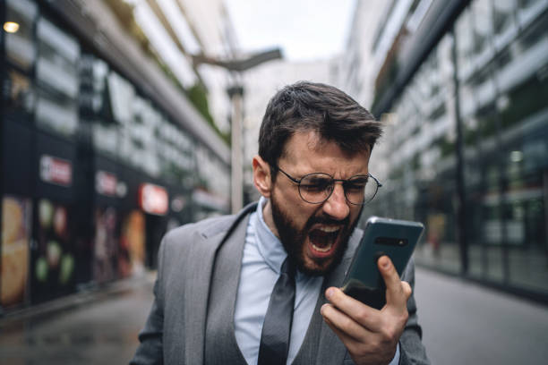 istock Young distraught businessman shouting while recording a voicemail on a mobile phone 1218452244