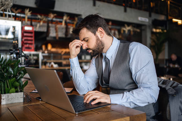 istock Tired businessman with a headache working from a cafe 1218452911