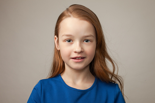 studio close-up portrait of a 9 year old girl with long brown hair in a blue t-shirt on a gray background