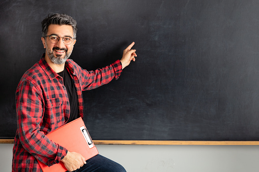 Adult man teacher standing on blackboard in classroom.