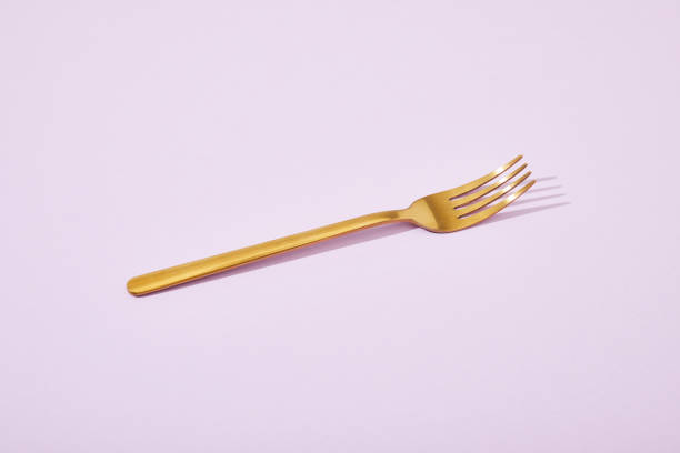 istock metal shiny golden fork on violet background 1218458580