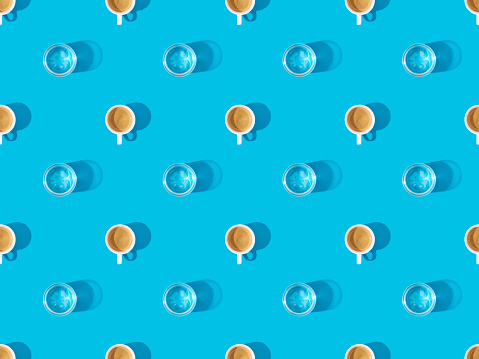 top view of cups of fresh coffee and glasses of water on blue, seamless background pattern