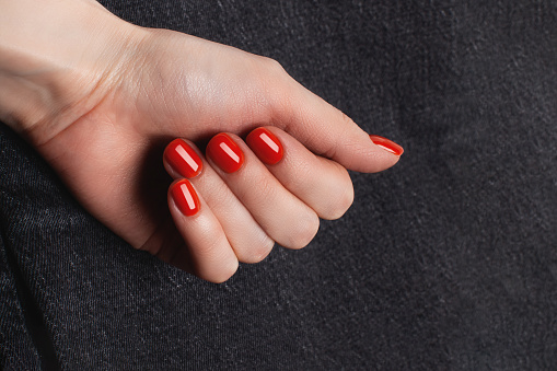 A hand with a red manicure on gray denim background.