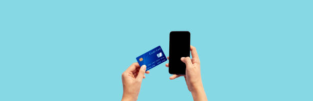 istock Woman hand holding blue credit card and using smart phone isolated on blue background, front side view. Blue bank-card design mock up. mobile payment ,online shopping concept 1218470452