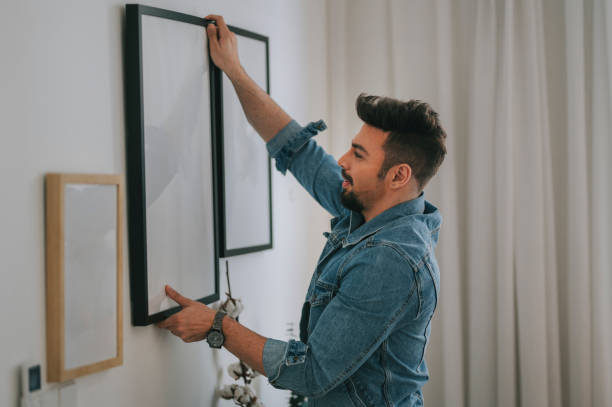 un homme du moyen-orient avec la barbe accrochant une peinture sur le mur à son salon - home decorating photos photos et images de collection