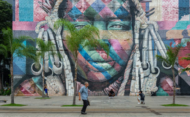 An unidentified man walks across the famous Olympic Boulevard of Rio de Janeiro with art mural called "Etnias" (Ethnicities) in the background Rio de Janeiro, Brazil - January 3, 2020: An unidentified man walks across the famous Olympic Boulevard in the Port Zone of Rio de Janeiro with art mural called "Etnias" (Ethnicities) in the background.That art work was designed by the artist Eduardo Kobras in 2016 and is considered the biggest graffiti in the world. The mural represents the native tribes from five continents: Huli (Oceania), Mursi (Africa), Kayin (Asia), Supi (Europe) and Tapajós (America). streetart stock pictures, royalty-free photos & images
