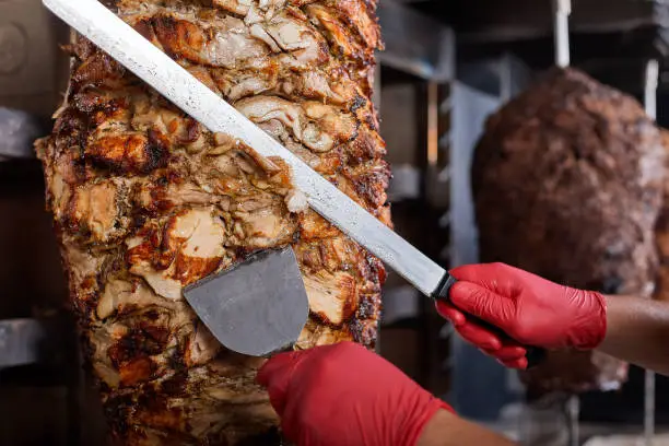 Fried meat on a skewer for cooking of donors or shawarma. Hands close-up cuts meat in thin slice